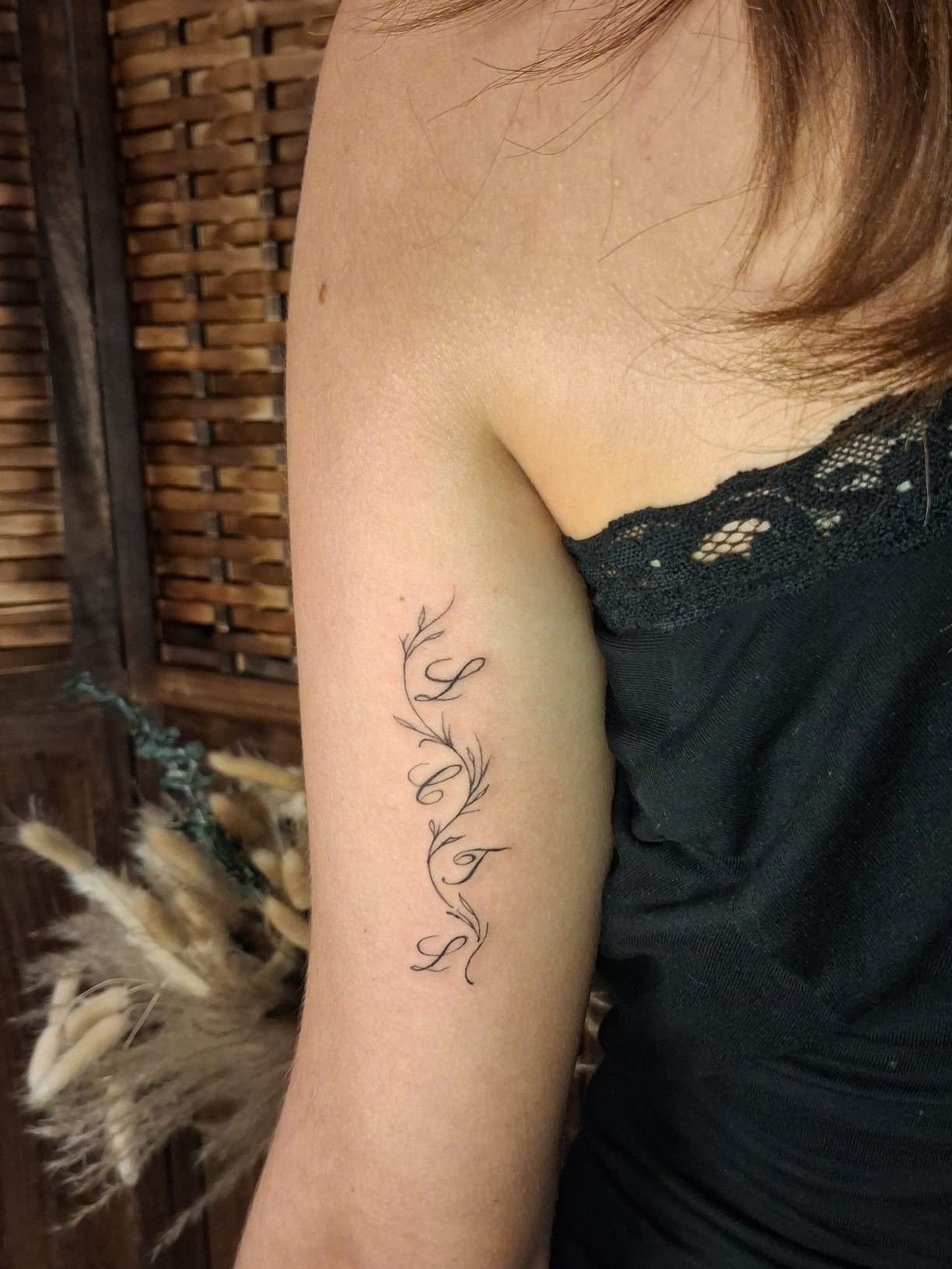 Fine branche en volutes, en trait fin, sur l’arrière du bras.