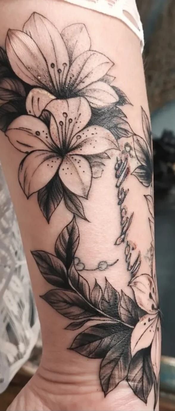 Grands lys et feuillages ombrés en black and grey sur l’avant-bras : un cover qui recouvre un ancien tatouage.