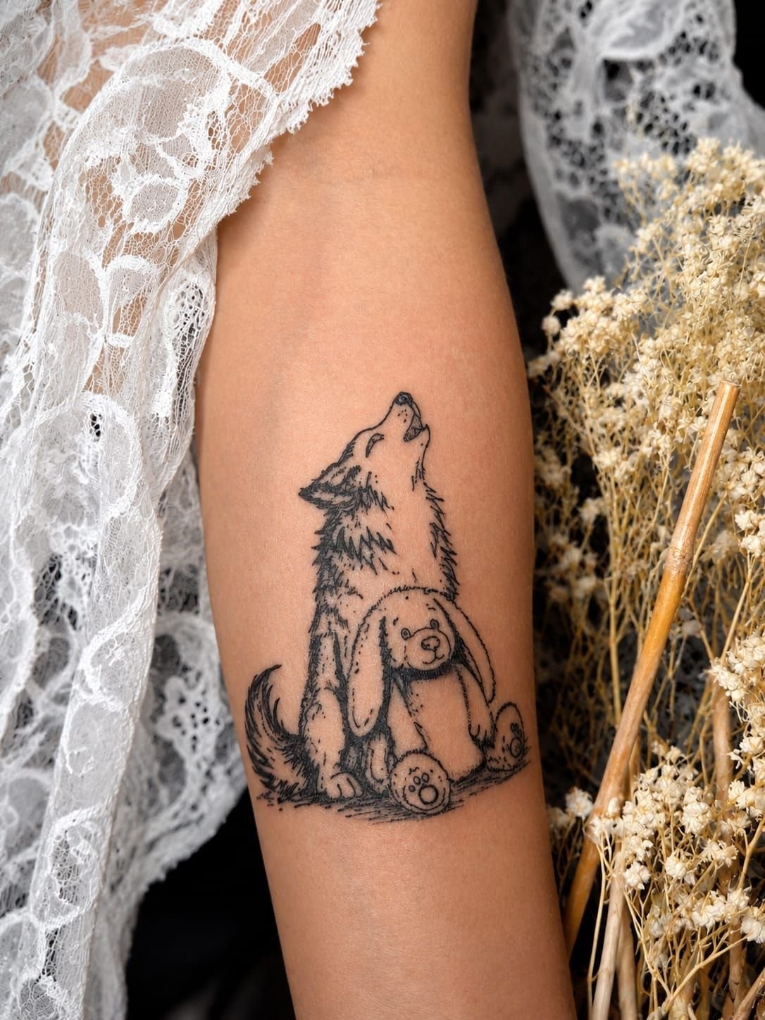 Louveteau qui hurle, assis contre une peluche lapin, en trait noir illustratif sur l’avant-bras.