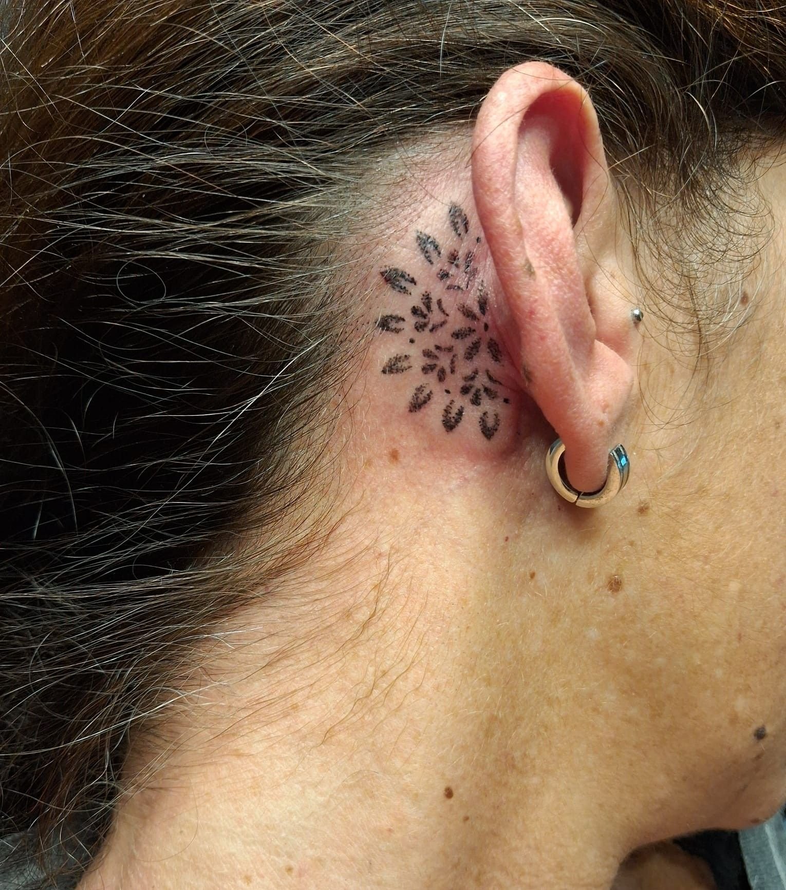 Petit mandala de pétales ombrés en points, derrière l’oreille.