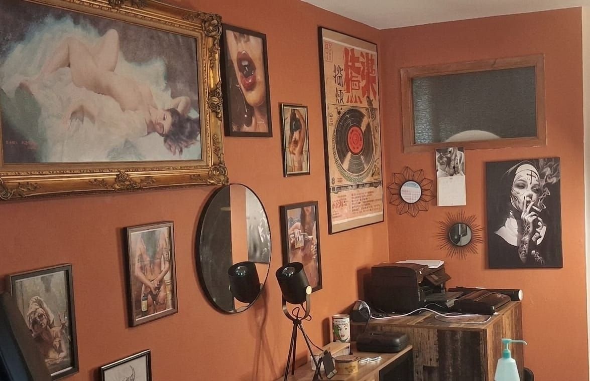 Le salon : mur terracotta couvert de cadres, un grand cadre doré, un miroir rond, des affiches, une commode en bois brut.