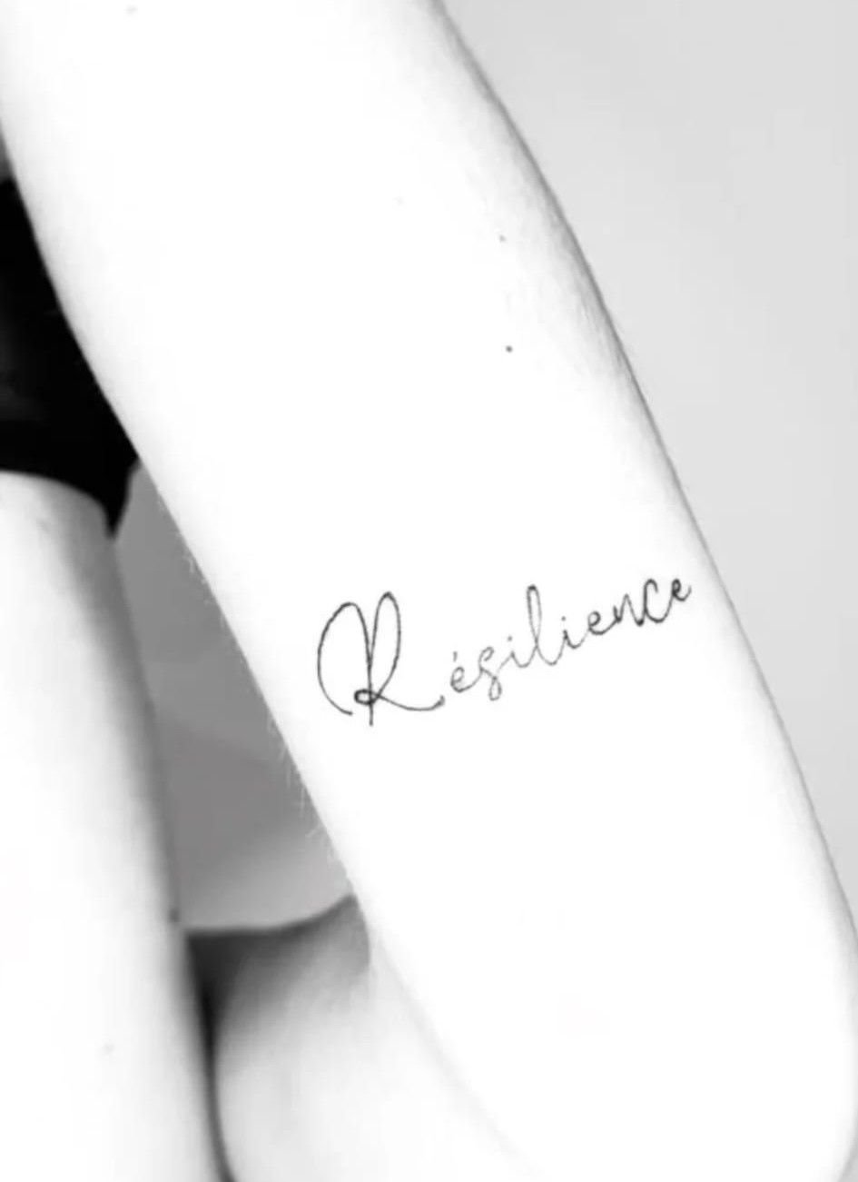 Le mot « Résilience » en écriture fine et calligraphiée sur le bras, photo en noir et blanc.